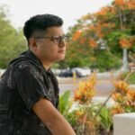Relaxed man with glasses in a Yucatan park surrounded by vibrant flora.
