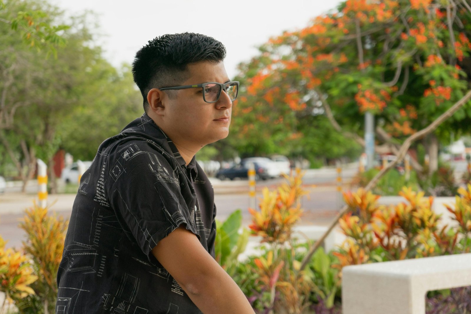 Relaxed man with glasses in a Yucatan park surrounded by vibrant flora.